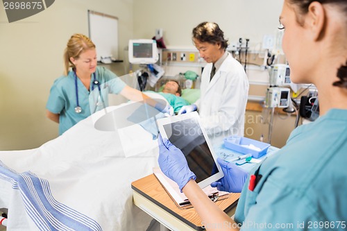 Image of Nurse Holding Digital Tablet While Colleague And Doctor Operatin