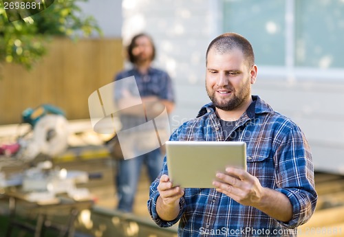 Image of Carpenter Using Digital Tablet With Coworker Standing In Backgro