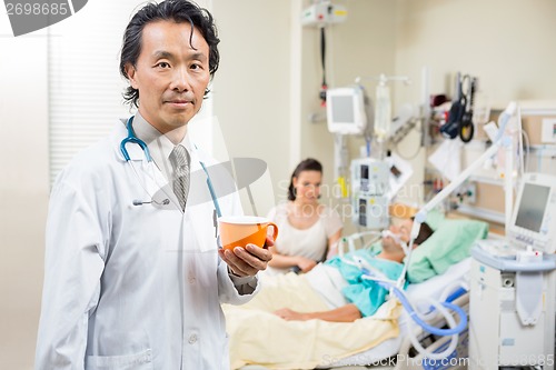 Image of Doctor Holding Coffee Cup With Patient Resting In Hospital