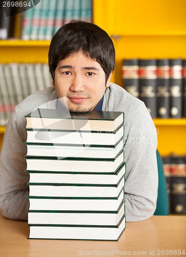 Image of Student Resting Chin On Stacked Books At Table In Library