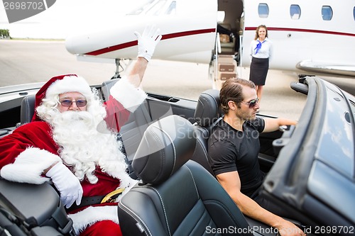 Image of Santa Waving Hand While Chauffeur Driving Convertible Against Pr