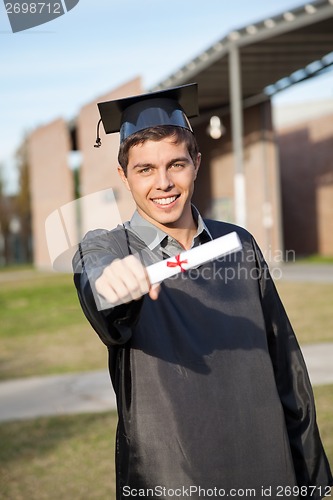 Image of Man In Graduation Gown Showing Diploma On University Campus