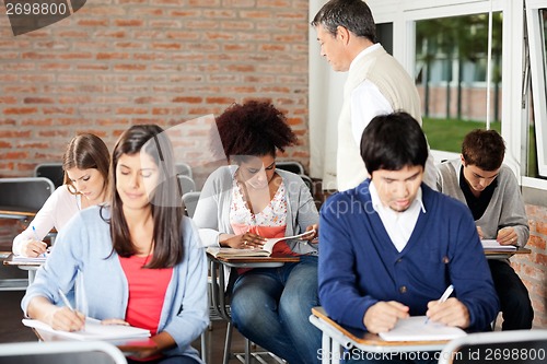 Image of Students Writing Exam While Teacher Supervising Them In Classroo