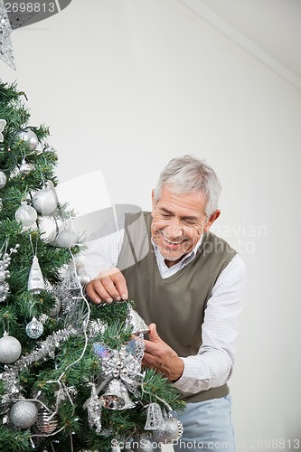 Image of Senior Man Decorating Christmas Tree With Silver Ornaments