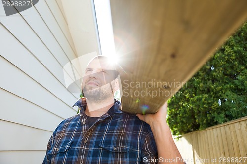 Image of Carpenter Carrying Plank At Construction Site