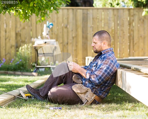 Image of Carpenter Messaging On Cellphone While Leaning On Wooden Frame