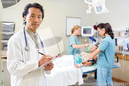 Image of Doctor Holding Clipboard With Nurses Examining Patient