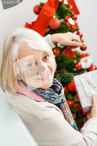 Image of Senior Woman Holding Present By Christmas Tree