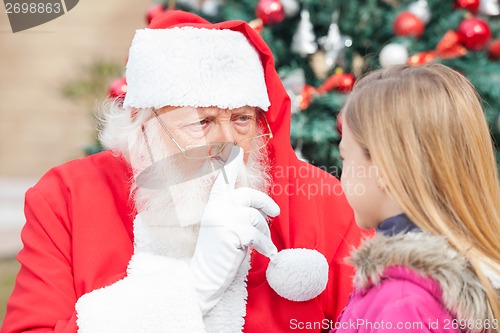 Image of Santa Claus Gesturing Finger On Lips While Looking At Girl