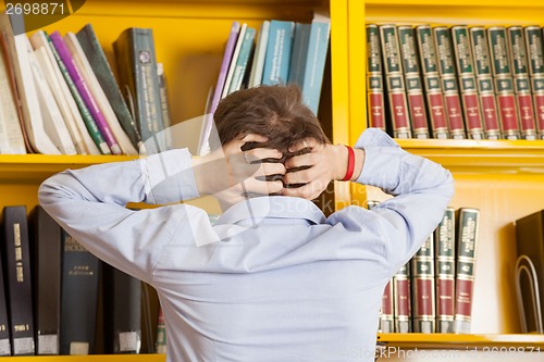 Image of Student Pulling Hair Against Bookshelf In University Library