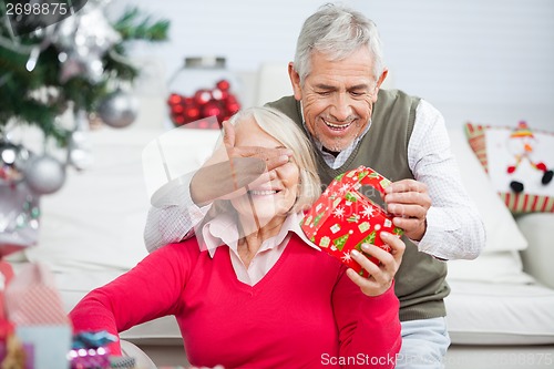 Image of Senior Man Covering Woman's Eyes While Giving Christmas Present