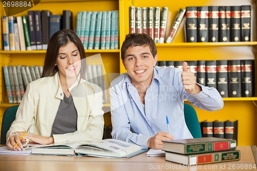 Image of Student Gesturing Thumbsup While Friend Reading Book In Library