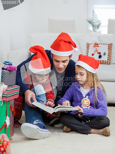 Image of Father And Children In Santa Hats Reading Book