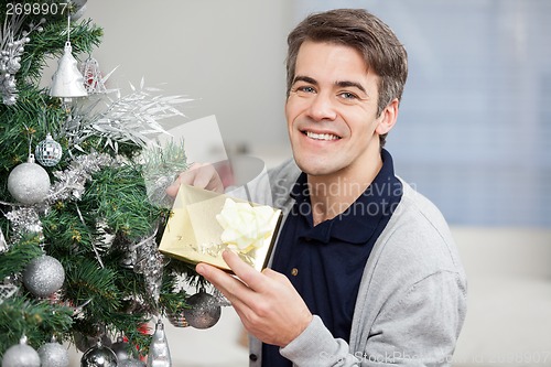 Image of Happy Man Holding Gift By Christmas Tree