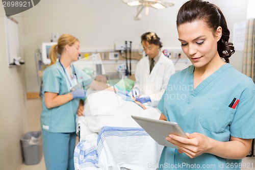 Image of Nurse Using Digital Tablet While Doctor And Colleague Operating