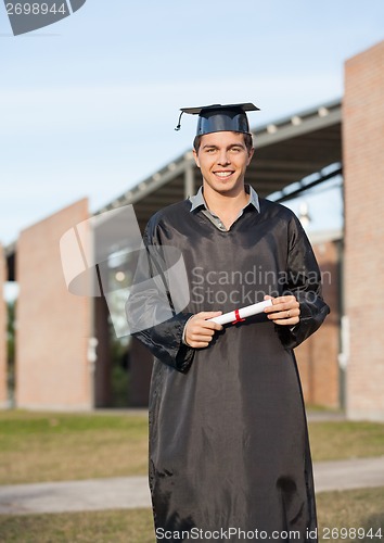 Image of Man In Graduation Gown Holding Diploma On College Campus