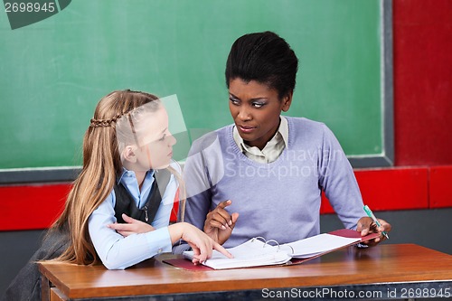 Image of Female Teacher Looking At Schoolgirl In Classroom