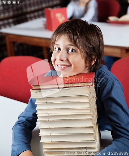 Image of Schoolboy Resting Chin On Stacked Books At Table