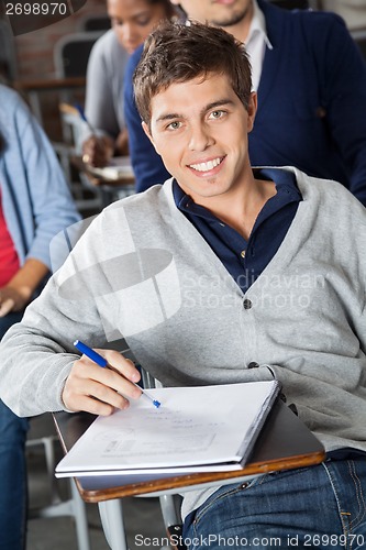Image of Man With Exam Paper Sitting At Desk In Classroom