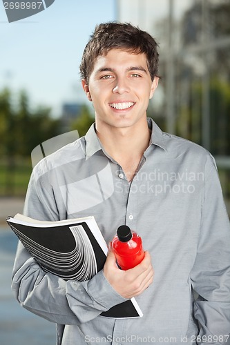 Image of Male Student With Juice Bottle And Book Standing On Campus