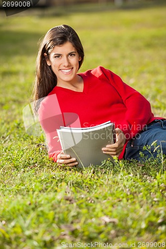 Image of Student Holding Books While Relaxing On Grass At Campus