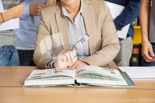 Image of Teacher Sitting At Table With Students Standing In Background