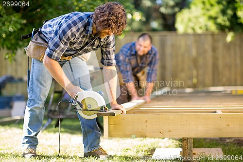 Image of Carpenter Cutting Wood With Handheld Saw While Coworker Helping