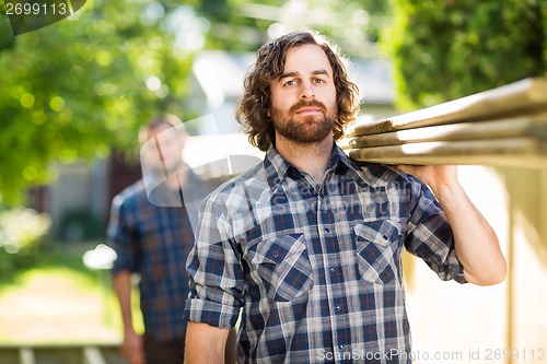 Image of Carpenter With Coworker Carrying Wooden Planks Outdoors