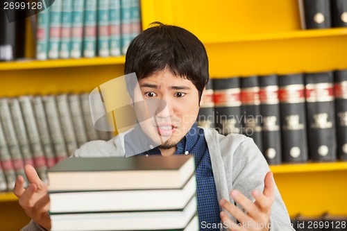 Image of Student Looking At Pile Of Books In University Library