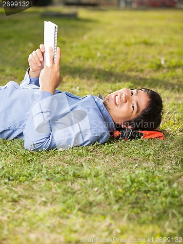 Image of Relaxed Man Holding Book While Lying On Grass At Campus