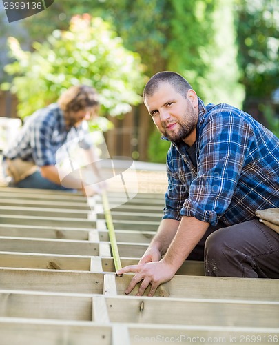 Image of Carpenter Measuring Wood With Tape While Coworker Helping Him