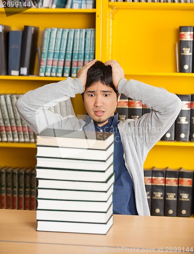 Image of Confused Man Looking At Stacked Books In Library