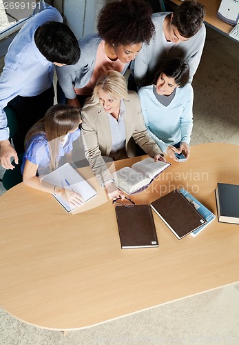 Image of Teacher Discussing With Students At Desk In Classroom