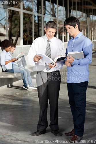 Image of Teacher And Student Discussing Over Book On University Campus