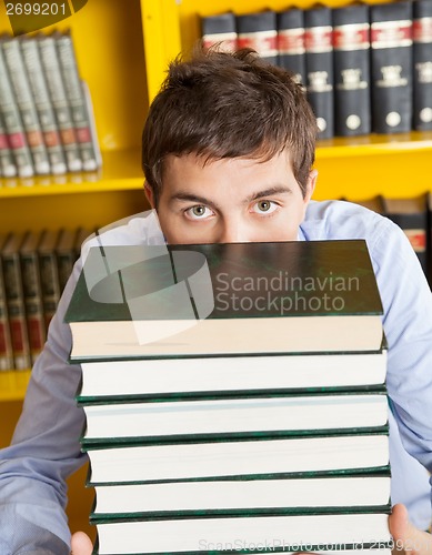 Image of Male Student Peeking Over Stacked Books In Library