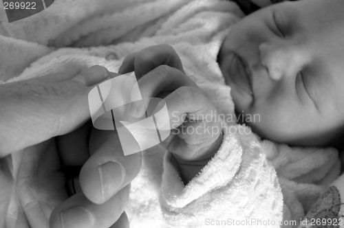 Image of newborn girl holding on to her daddy's finger while sleeping