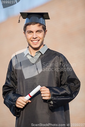 Image of Happy Man In Graduation Gown Holding Certificate On Campus