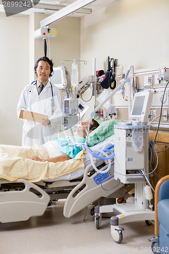 Image of Doctor With Patient's Report Standing By Bed