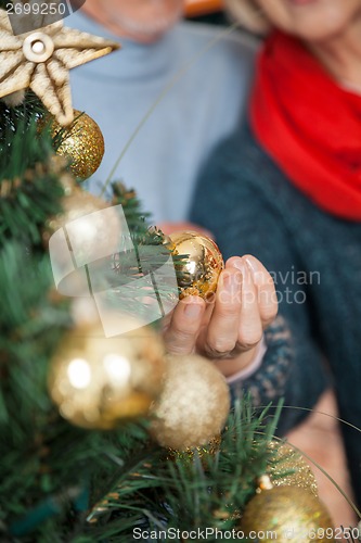 Image of Couple Selecting Baubles Hanging On Christmas Tree At Store