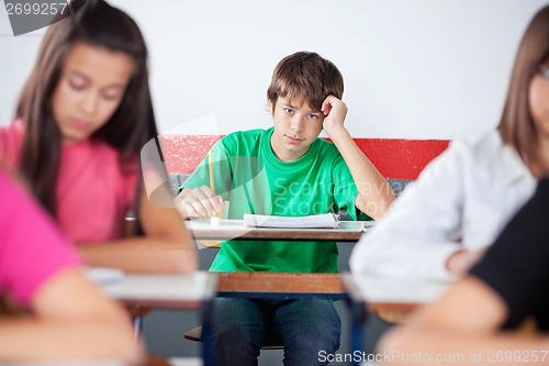 Image of Teenage Male Student Leaning On Desk At Classroom