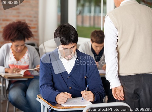 Image of Students Giving Exam While Teacher Supervising Them In Classroom