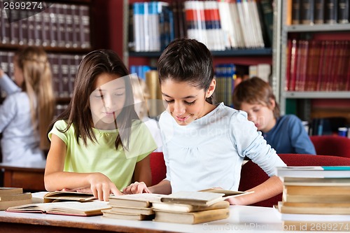 Image of Schoolgirls Reading Book Together At Table In Library