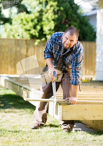 Image of Mid Adult Worker Cutting Wood With Saw At Construction Site