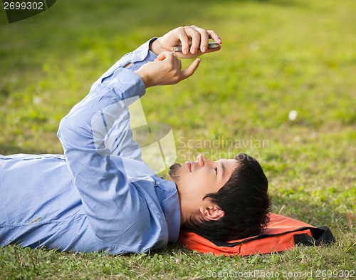 Image of Man Using Mobilephone While Lying On Grass At Campus