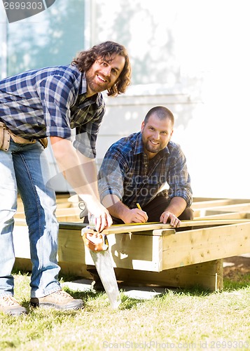 Image of Workers Measuring Wood Together At Construction Site