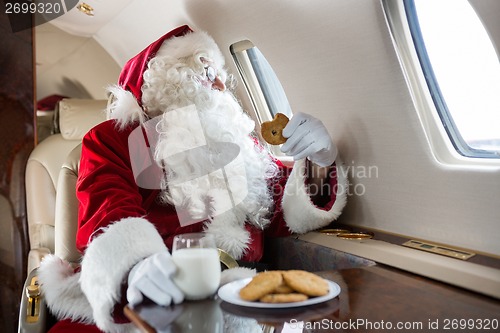 Image of Santa Holding Cookie While Looking Through Private Jet's Window