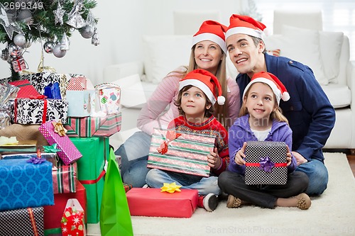 Image of Family In Santa Hats Sitting By Christmas Presents