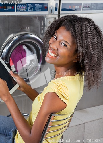 Image of Woman Holding Digital Tablet Sitting At Laundromat