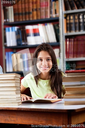 Image of Happy Schoolgirl Sitting With Stack Of Books In Library