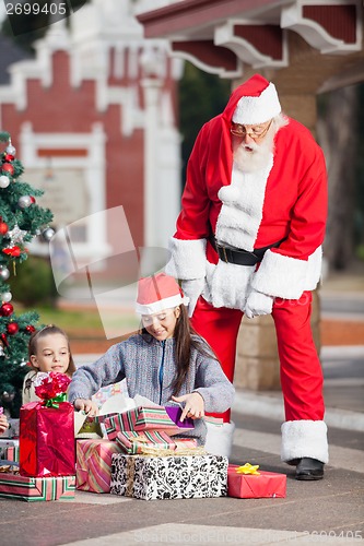 Image of Santa Claus Looking At Children Opening Christmas Presents